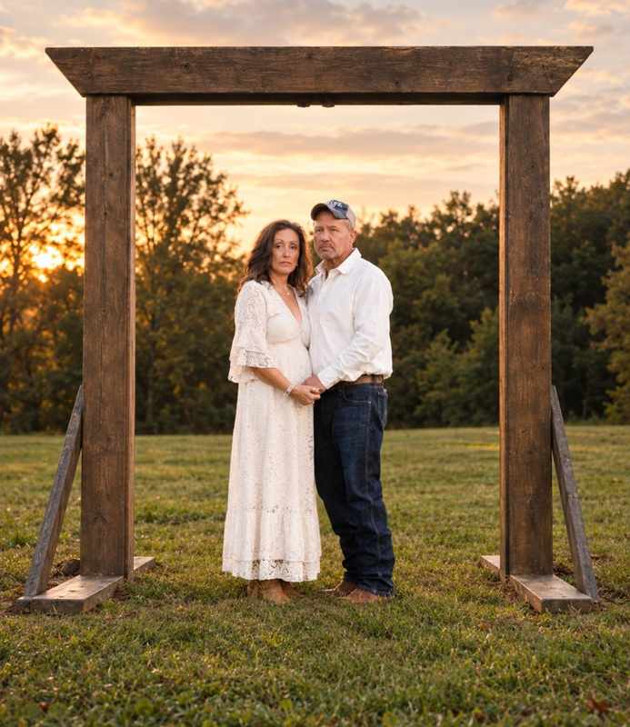 Anniversary couple framed by a rustic wooden arch at sunset