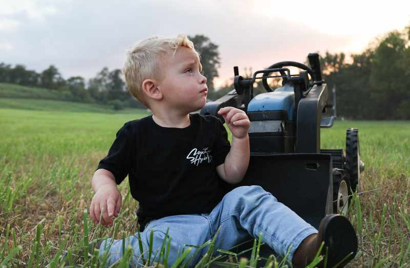 Young boy sitting beside a small blue tractor at sunset