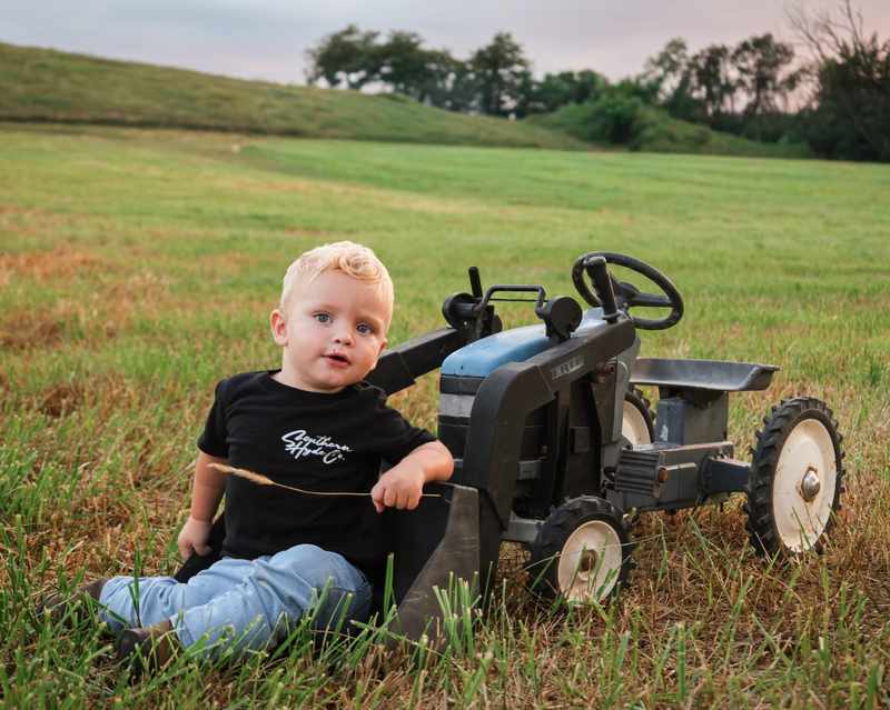 Young boy sitting beside a small blue tractor in a country field