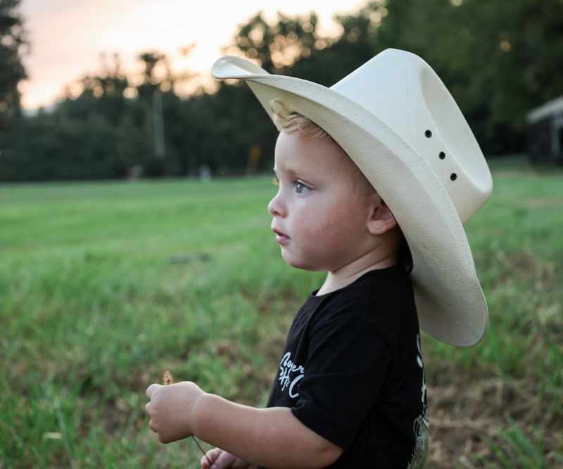 Side profile of a young boy wearing a cowboy hat in a field