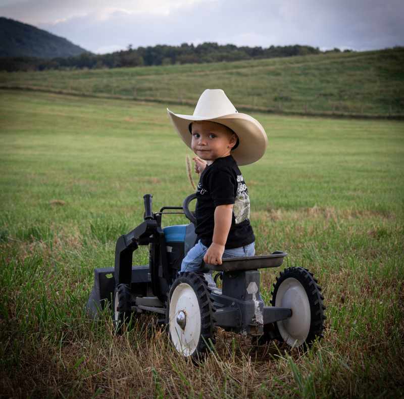 Young boy in a cowboy hat sitting on a small tractor with mountains behind him