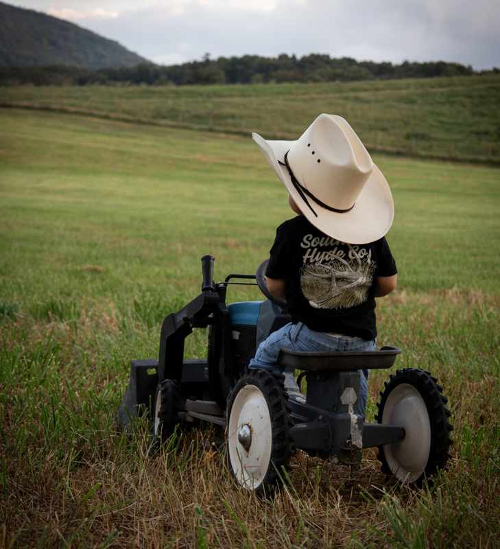 Young boy sitting on a small tractor with his cowboy hat tipped forward