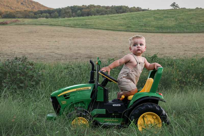 Young boy kneeling on a green John Deere toy tractor