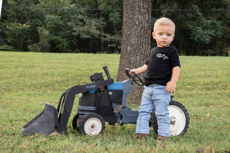 Young boy standing beside a small blue tractor in the yard