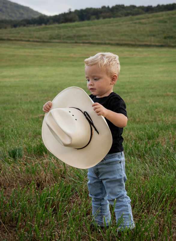 Young boy holding a large cowboy hat in a field