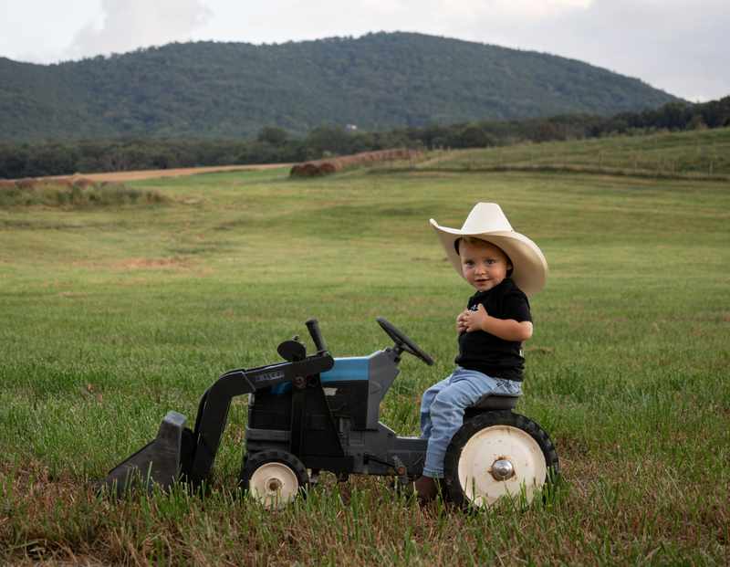 Young boy wearing a cowboy hat on a small tractor with a mountain backdrop