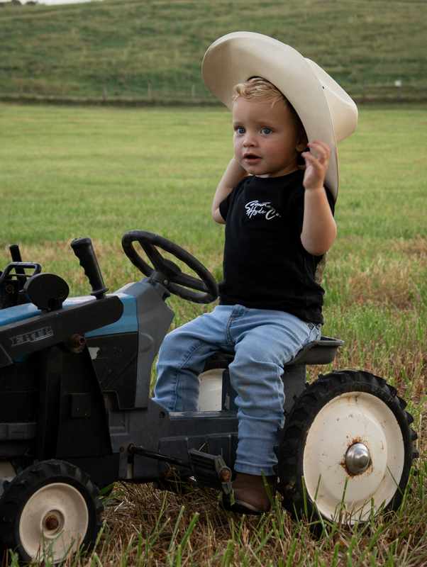 Young boy adjusting his cowboy hat while sitting on a small tractor